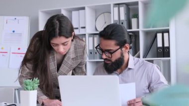 Odaklanmış meslektaşlar, Kafkasyalı ve Hintli ofis çalışanları, ekip çalışması ve iş birliği. İş evraklarıyla meşgul olmak, dizüstü bilgisayar kullanmak, konuşmak..