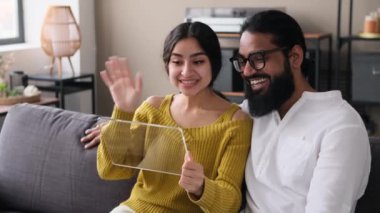 Mutlu Hintli çift video aracılığıyla konuşuyor, el sallayarak selamlıyorlar, modern cam tablet bilgisayar kullanıyorlar. Gelecekçi aygıt ekran modeli, modern teknoloji konsepti.