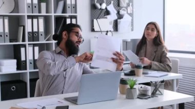 Çok uluslu iş arkadaşları, Hintli erkek ve Kafkasyalı kadın büroda birlikte çalışırlar, belgeleri analiz ederler, profesyonel araştırmalar yaparlar, birbirlerine danışırlar..