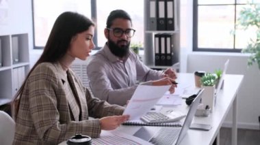 Kafkasyalı kadın ve Hintli adam da dahil olmak üzere iş ekibi, konuşuyorlar, evraklarla uğraşıyorlar, ofiste birbirlerine danışıyorlar. İş arkadaşı sohbeti. Ortaklık ve işbirliği kavramı.