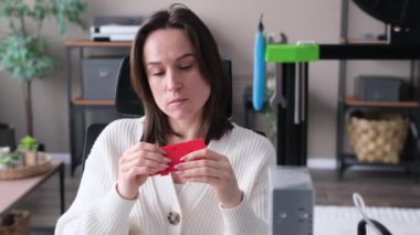 Genç beyaz kadın tasarımcı ev atölyesinde dizüstü bilgisayar ve 3D yazıcı ile çalışıyor. Araştırmalar basıldı, proje geliştiriliyor. DIY kavramı.