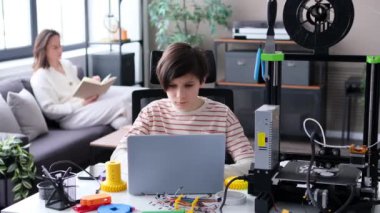 3D baskılı çark detaylarını inceleyen düşünceli bir öğrenci, yazıcı kalitesini kontrol ediyor. Ev atölyesinde dizüstü bilgisayarla öğrenme, araştırma ve geliştirme.