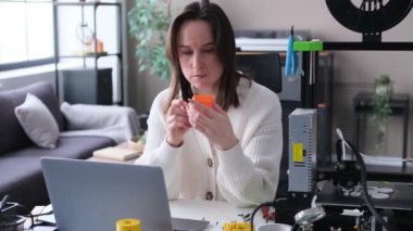 Üç boyutlu yazıcı, dizüstü bilgisayar ve 3D yazıcı ile ev atölyesinde çalışan düşünceli beyaz kadın tasarımcı. Prototip ve araştırma, yerli üretim kavramı.