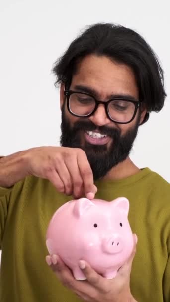 Медленный Снимок Улыбающегося Бородатого Молодого Человека Вставляющего Монеты Розовую Копилку — стоковое видео