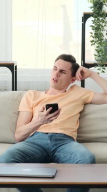 Kanepede oturan adamın yüz ifadesi hayal kırıklığı ve can sıkıntısıyla doluydu. Elinde bir telefon tutuyor ama bu bile onu tembellik duygusundan alıkoymuyor..