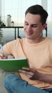 Sıcak bir gülümseme ile genç bir adam, rahat bir kanepede otururken not defterine not almaya dalmış. Odanın sıcacık atmosferi, o dikkatle görevine odaklanırken dingin atmosfere katılıyor..