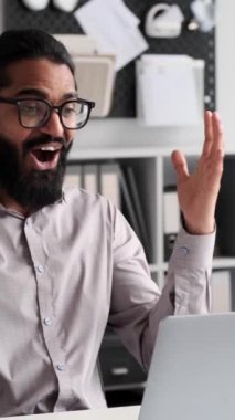 Sevinçli iş adamı, iş kıyafetleri içinde sıralanmış, ofis masasında elde ettiği başarıları bir dizüstü bilgisayarla sevinçle kutluyor. Etkileyici jestler ve keyifli ifadeler bir başarı hissi taşır..