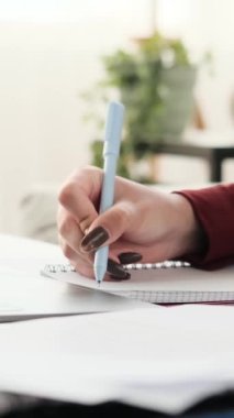 Yakın plan çekimde, genç bir kızın elleri dizüstü bilgisayarın klavyesinde ustaca yazarken aynı zamanda kalem kullanarak not alırken görülebilir..