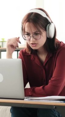 Çalışmalarına dalmış genç bir kız, çevrimiçi bir video dersine dikkatle katılırken kulaklık takıyor. Eğitimsel içeriği özümser, notlar alır ve materyallerle ilgilenir..