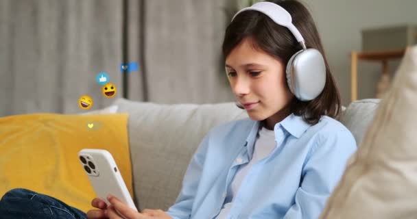 Pozytywny Biały Uczeń Słuchawkach Przy Użyciu Telefonu Latającymi Emoji Siedząc — Wideo stockowe