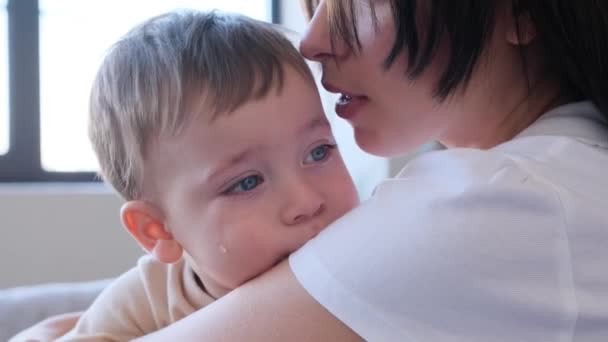 紧贴着一个哭哭啼啼的幼儿的画像 脸上含着泪水 坐在母亲的手上 妈妈抚摸着 拥抱并抚慰着她可怜的小儿子 — 图库视频影像
