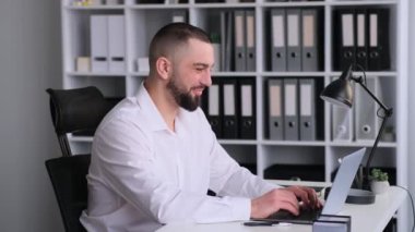 Ofiste dizüstü bilgisayarla çalışırken kameraya bakan olumlu beyaz iş adamının portresi. Başarılı patron, girişimci, yönetmen..