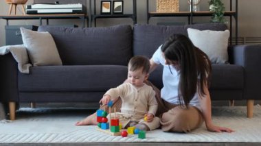 Mutlu beyaz anne ve küçük oğlu birlikte tahta oyuncaklarla oynuyorlar. Oturma odasının zemininde oturuyorlar. Ev içi eğlence aktivitesi, oyun eğitimi.