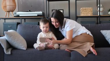 Kafkasyalı anne ve yeni yürümeye başlayan oğlu cep telefonlarıyla internetten video izleyip oturma odasındaki kanepede birlikte oturuyorlar. Çevrimiçi karikatür veya eğitim videoları.