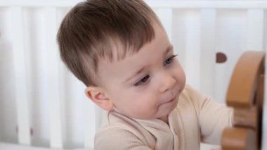 Oyun odasındaki beşikte tek başına tahta oyuncakla oynayan meraklı ve ilgilenen beyaz bir çocuğun portresi. Olumlu bebek portresi.