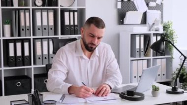 Belgeler ve dizüstü bilgisayarla çalışan, ofisinde oturan dalgın bir Kafkasyalı ofis çalışanı. Kağıtları düzenler, iş araştırmaları ve muhasebe yapar.