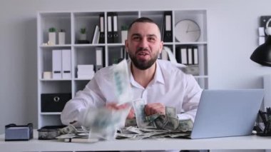Şaşırmış, mutlu, Kafkasyalı bir işadamının portresi para başarısını ve zaferini kutluyor, ofiste masa başında çalışıyor. Finansal büyüme kavramı.