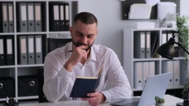 Ciddi bir beyaz erkek ofis çalışanı planlama programı ya da gündem, not defterine yazma, hazırlık takvimi, beyin fırtınası ve düşünme.