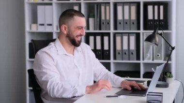 Başarıyı veya zaferi kutlayan neşeli Kafkas işadamı, ofiste çalışırken dizüstü bilgisayardan iyi haberler alıyor. Başarılı bir anlaşma ya da sonuç kavramı.