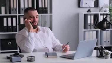 Arkadaş canlısı beyaz erkek ofis çalışanı cep telefonu kullanıyor müşteriyle konuşuyor, ofisinde oturuyor. Satış uzmanı danışman müşteri.