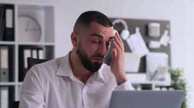 Laptop ve facepalizmle çalışan, ofiste oturan hayal kırıklığına uğramış beyaz bir adamın portresi. Hata veya hatalara tepki, başarısızlıktan sersemlemiş.