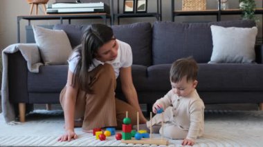 Bebek ve mutlu anne oyuncaklarla oynuyor, eğitim ve oyun süreçleriyle meşgul, boş zamanlarını evde oturma odasında yerde oturarak geçiriyor..