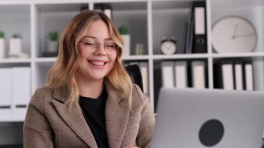 Ofis molasında dinlenen neşeli beyaz iş kadını bilgisayarla video görüşmesinde gülüyor ve konuşuyor. Ofis boş zaman ve eğlence konsepti.