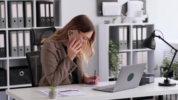 コカシアの女性オフィスワーカーは クライアントと電話をしたり ラップトップを使ったり 書類を作ったりして 現代のオフィスで机の上に座ったりしている リモートコンサルティング プロアドバイザー — ストック動画
