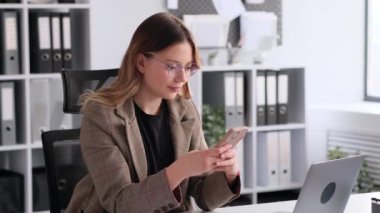 Beyaz kadın çalışan ofis molası sırasında akıllı telefonla dinleniyor. Sosyal medya uygulamasında e-posta ya da haber okumak, sohbet etmek ya da mesajlaşmak.