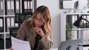Ofiste çalışan düşünceli, beyaz, serbest çalışan bir kadın bilgisayar kullanarak evrakları inceliyor. Mali büyümenin analizi, iş bankacılığı ve denetimde çalışma.