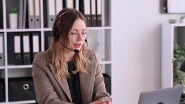 Ofiste çalışan, kulaklık takan ve dizüstü bilgisayar kullanan beyaz kadın yardım hattı danışmanı. Çevrimiçi sohbet ya da tartışma, video çağrısı kavramı.