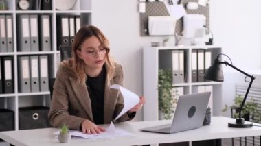 Ofiste laptopla ve kağıtlarla çalışan konsantre beyaz kadın. Profesyonel girişimci iş muhasebe veya planlama projesinde yer aldı.