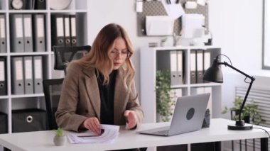 Acele eden Kafkasyalı kadın ofis çalışanı ofiste evrak işi yapıyor, dizüstü bilgisayar kullanıyor. Son teslim tarihine yetiş, masa başında iş belgelerini incele..