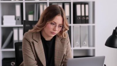 Ofiste dizüstü bilgisayarla çalışan yorgun ya da sıkılmış beyaz kadın ofis çalışanı. Sıkıntı, üzüntü, yorgunluk konsepti. Yakma ve iş sorunları.