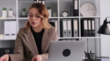 Modern ofiste dizüstü bilgisayar kullanarak çevrimiçi konferans sırasında evrak işleriyle uğraşan kadın bir ofis çalışanı. Patron çalışanlarla online konuşuyor..