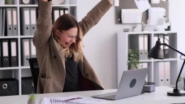 Dizüstü bilgisayarla çalışan ve ofisteki başarıyı kutlayan beyaz bir kadın. İyi haber, galibiyet, zafer, finansal büyüme kavramı.