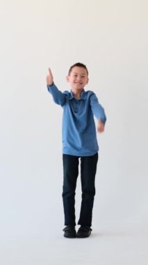 İyimser Asyalı genç okul çocuğu iki eliyle işaret gibi görünüyor ve beyaz arka planda dans ediyor. Kabul jesti. Dikey video.