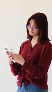 Cep telefonlu, internetten sohbet eden ya da internette gezinen, beyaz arka planda iyi haberler alan beyaz kız hayrete düştü. Dikey video.