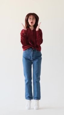 Şaşırmış Kafkasyalı genç kız, beyaz arka plana karşı zafer ve dansı, zaferi ya da sürprizi kutluyor. Olumlu tepki. Dikey video.