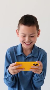 Beyaz arka planda cep telefonuyla video oyunu oynayan heyecanlı Asyalı çocuk. Online eğlence ve oyun konsepti. Dikey video.