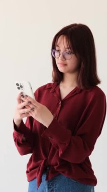 Akıllı telefonlu, internete takılan ve beyaz arka planda gülen neşeli beyaz kız. Dijital online eğlence. Dikey video.