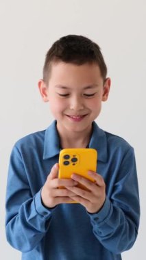 Arkadaş canlısı Asyalı genç çocuk cep telefonunu beyaz arka planda online eğlence için kullanıyor. İnternet konseptine göz atıyorum. Dikey video.