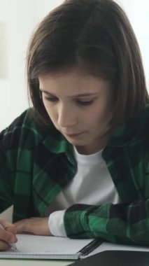 Özenli ve odaklanmış beyaz bir çocuğun portresi. Ev ödevi yaparken evde masa başında oturuyor. Dikey video.