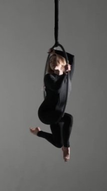 Beyaz kadın profesyonel akrobatik dansçı gri arka planda asılı havada dans gösterisi yapıyor. Dikey video.