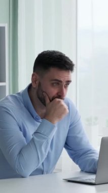 Ofiste dizüstü bilgisayarla çalışan düşünceli Kafkasyalı serbest çalışan bir erkek. İş çözümleri aramak, şirket stratejisini geliştirmek ve analiz etmek. Dikey video.