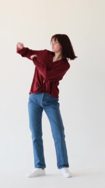 Beyaz arka planda müzik eşliğinde mutlu bir şekilde dans eden gülümseyen beyaz kız. Eğlenceli eğlence, dans aktiviteleri. Dikey video.