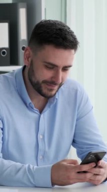 Ofis molasında cep telefonunu kullanırken, Kafkas erkek serbest çalışanı iyi haberler alıyor. Başarı ve haykırışı kutluyoruz. Dikey video.