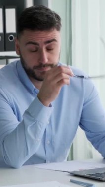 Ofiste dizüstü bilgisayarla çalışan yorgun beyaz bir erkek. Gözlüklerini çıkarır ve gözlerini ovar. İnternete göz atmak, başlangıçta çok çalışmak. Dikey video.