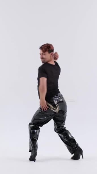 白い背景の上に高ヒールと革のズボンでエネルギッシュな流行ダンスのパフォーマンスを示す特別な白人男性 バーティカルビデオ — ストック動画