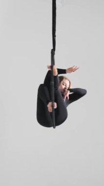 Beyaz arka planda asılı hava çemberi üzerinde jimnastik yapan beyaz bir kadın. Uçan dans ya da akrobatik performans konsepti. Dikey video.